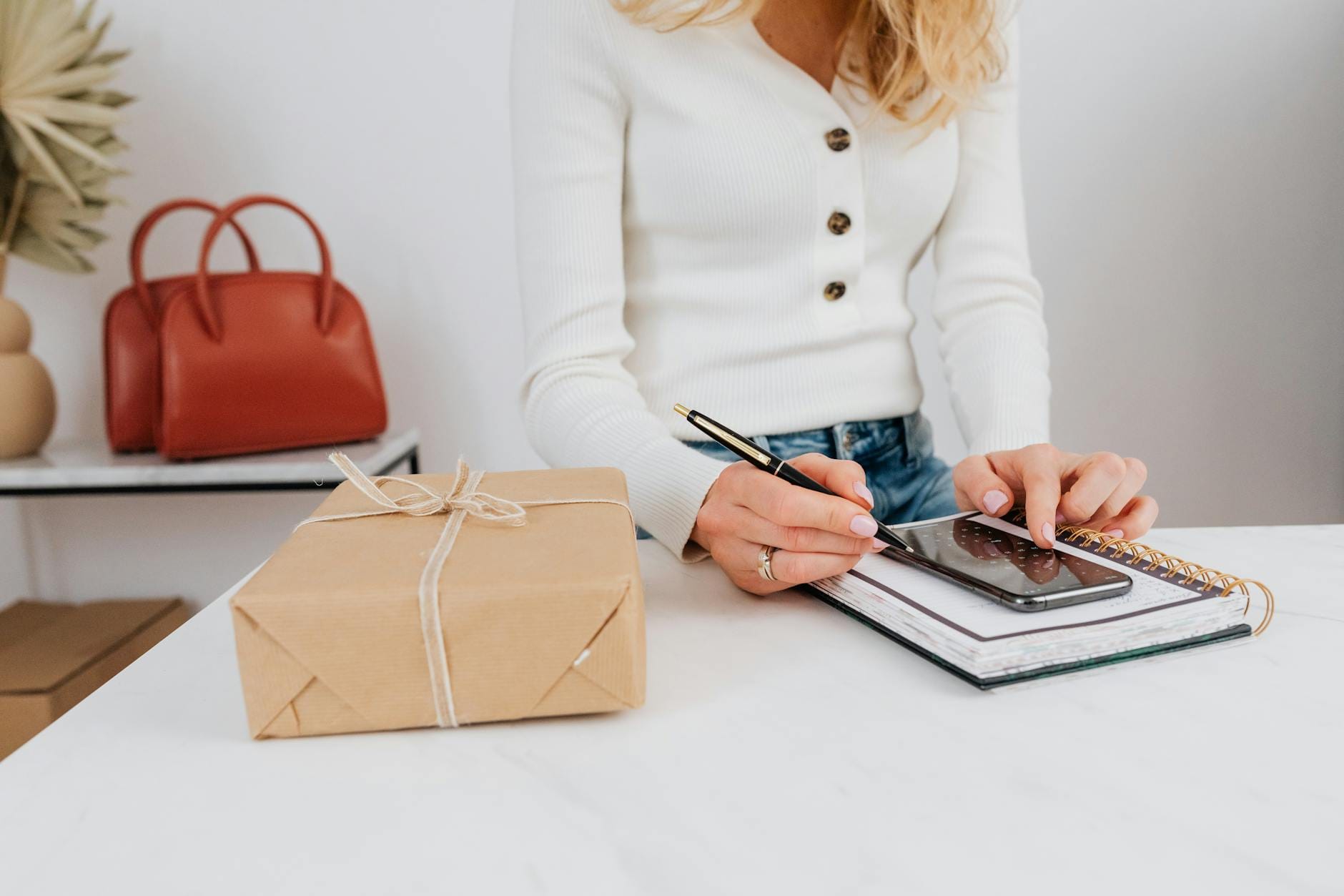 Kobieta pisze na smartfonie nad notesem przy pudełku z prezentem