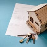Miniaturowy drewniany domek, klucze i umowa najmu mieszkania